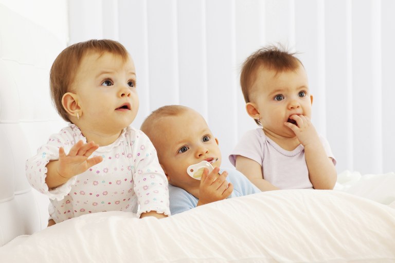 Drei Babys im Bett sitzend